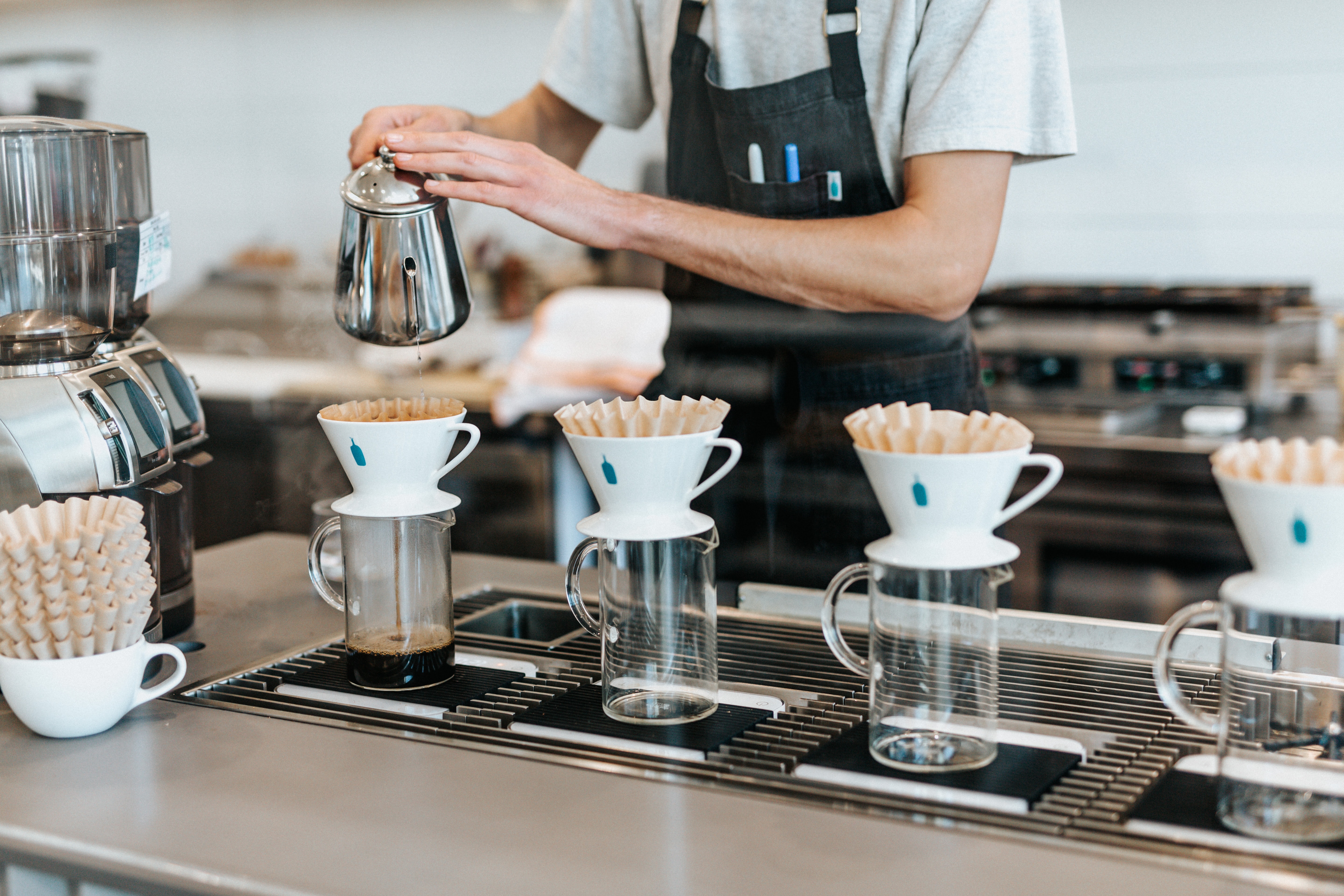A barista pours coffee into four Blue Bottle Coffee filters.