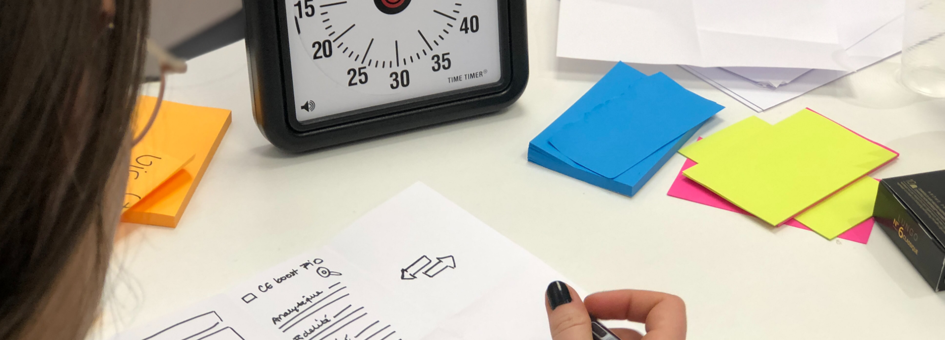A young women takes part in a Active Eights activity at her desk, where there are also post-it notes and a timer.