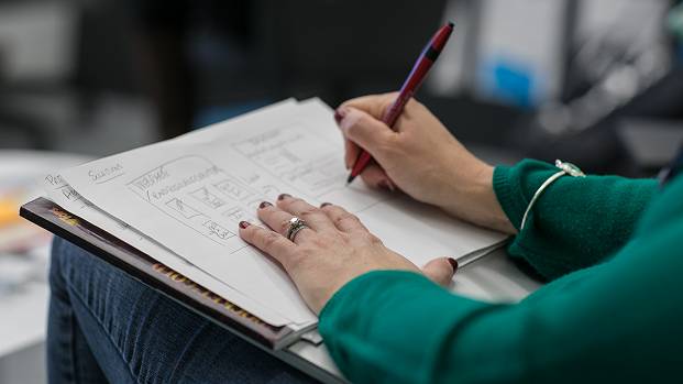 A person in a green jumper sketches out ideas on an A3 piece of paper.