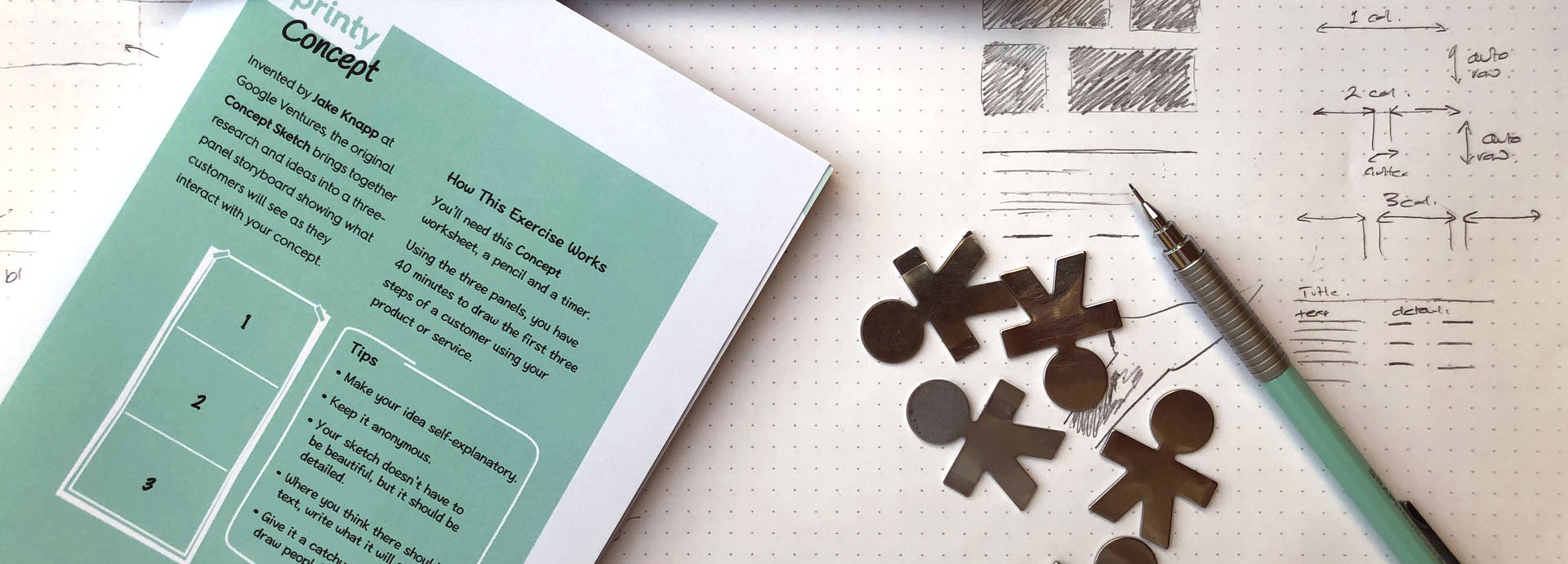 A hand holds a small humanoid metal cutout above a couple of worksheets laid out on a table.